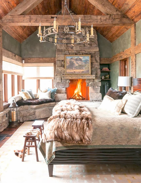 Luxurious cabin inspired bedroom with a stone fireplace, fur throw and a window seat