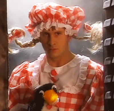 Arnold Rimmer from Red Dwarf in gingham outfit with pig tails and "Mr Flibble" the penguin glove puppet