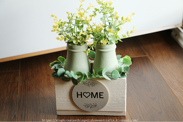 Painted light green glass bottles with faux floral and greenery displayed in a white wooden box