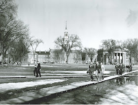 A photograph of men on The Dartmouth campus, walking along boards to avoid standing water.