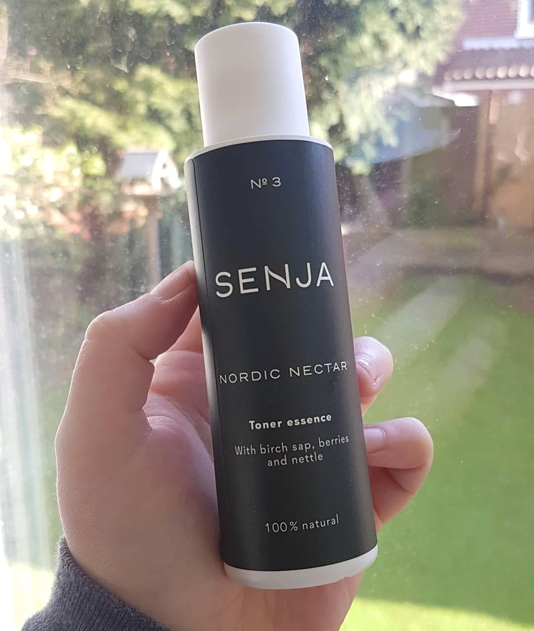 Nordic Nectar Toner from Finnish green beauty brand Senja held up in a hand in front of a window