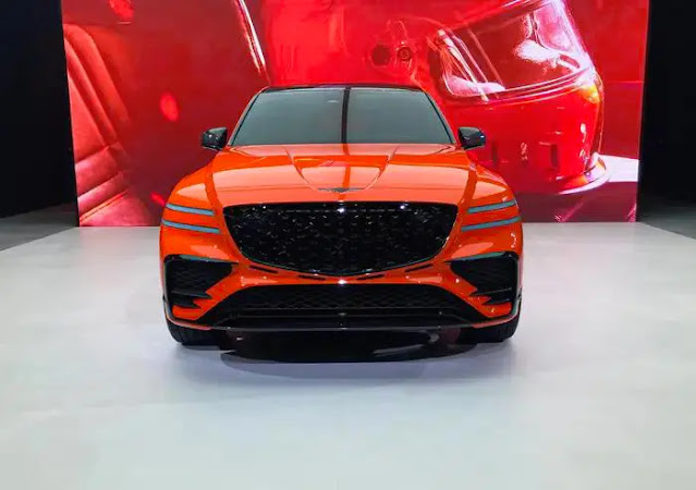 An orange Genesis GV80 Coupe concept SUV shown from the front, with a red backdrop.