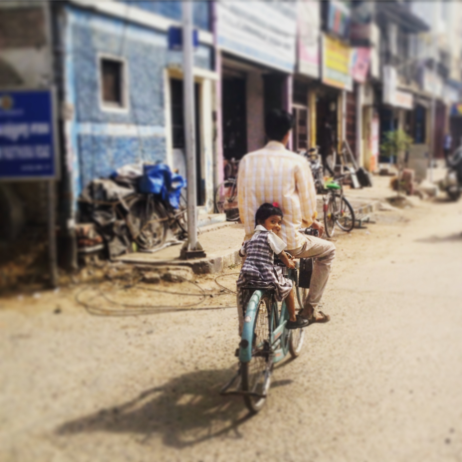 A girl sits on the back of a bicycle in an Indian village