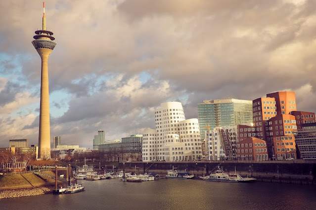 auf dem Foto ist die Skyline der Landeshauptstadt Düsseldorf, NRW zu sehen. Man sieht den Rhein, den Medienhafen, Boote und die Stadt bei bewölktem Himmel.