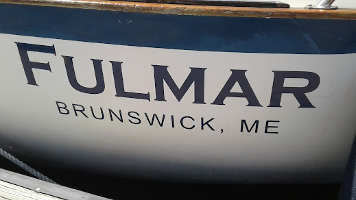 Blue boat lettering on a white boat.  It says "Fulmar" on the top line and "Brunswick ME" on the second line.