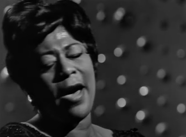 Close up of Ella Fitzgerald singing on a Swedish TV show in 1963. Her eyes are closed as she sings.