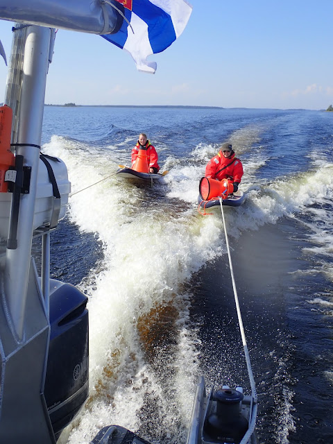 Kaksi kahluupisteen tekijää istuu sup-laudoillaan, joita vene hinaa. 