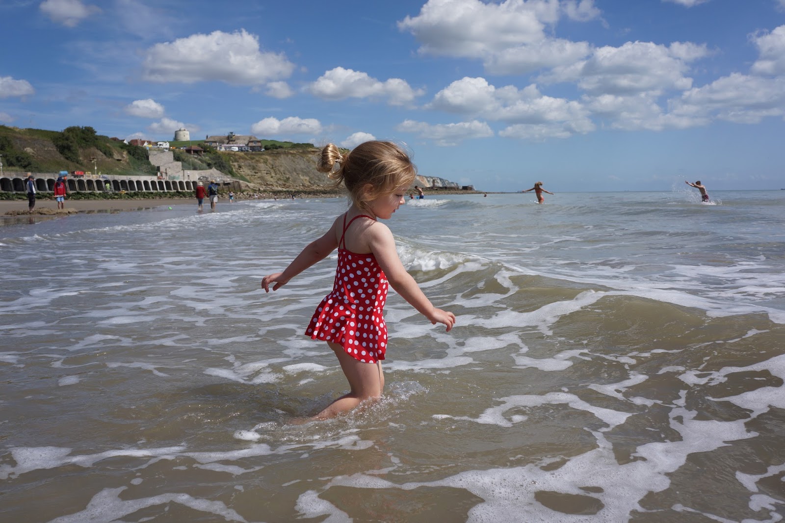 toddler in a red bathing suit wading into the sea