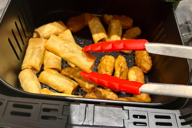 Open air fryer drawer showing perfectly crisped spring rolls