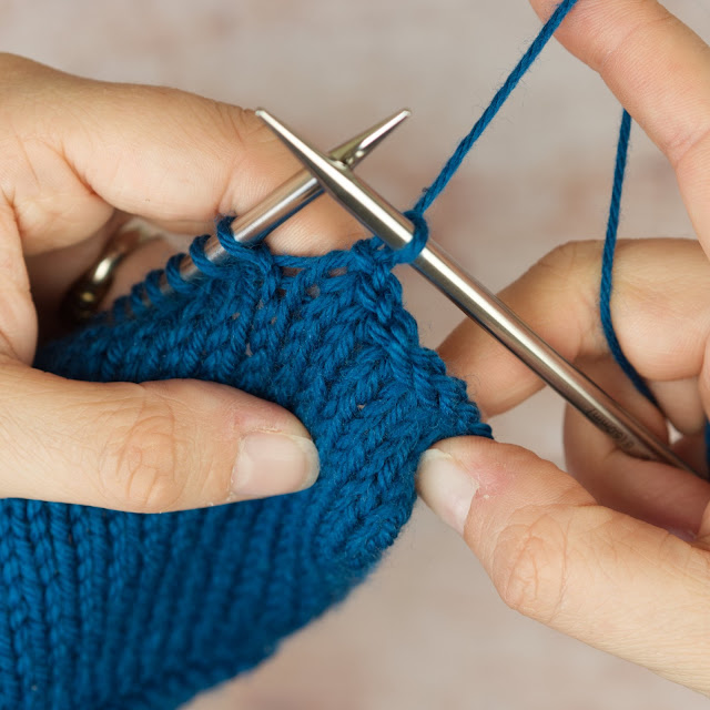 hands holding blue knitting and an inch of icelandic bind off worked