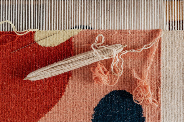 Woven tapestry fabric on a loom with an intricate pattern.