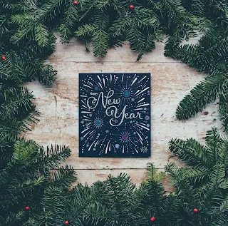 A ring of fir branches surrounding a picture of fireworks and the words Happy New Year!