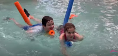 Picture of two happy Adaptive Swimming children paddling on noodles