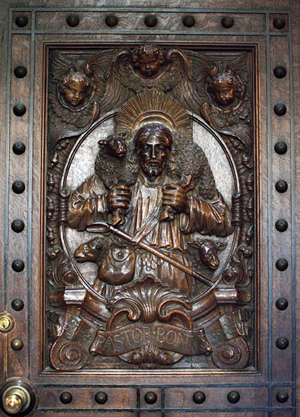 Hand carved wood door showing Jesus Christ carrying a sheep across his shoulder with the words Pastor Bonus carved below