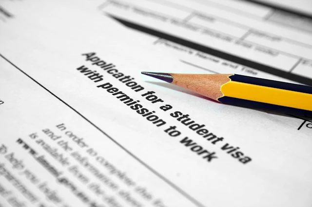 A close-up shows a section of a form titled "Application for a student visa with permission to work." A sharpened pencil with a natural wood barrel and blue and yellow stripes rests on the form, pointing towards the title. The form includes lines and spaces for filling in information.