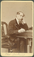 A photograph of Charles Dickens seated at a desk.