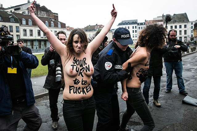 Półnaga aktywistka Femenu z rękoma wyciągniętymi w górę i napisem na torsie Your turn to be fucked