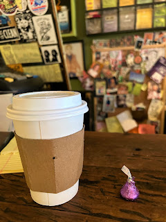A small coffee in a paper cup with a Hershey's Kiss next to it on the counter at Gleaner's Café