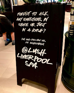 A black rectangular sign with @lushliverpoolspa in white font on a bright background