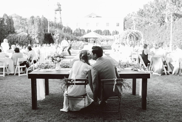 bride and groom sitting at a full olive garland table for their classic white garden wedding in utah