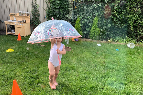 girl holding umberella outside next to a mud kitchen