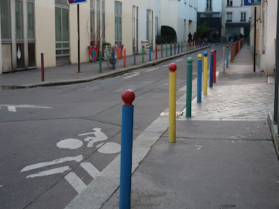 Paris street Allee Verte; buildings across the street, a line of colorful, slender bollards running down this side.