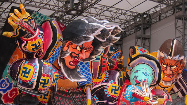 Colorful parade displays in the style of historic Japanese art, featuring large swastikas.