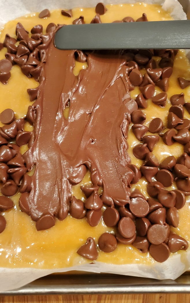 spreading chocolate on the coconut filling for mound cookie bars