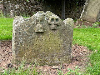 A small gravestone at Spott with a primitive style skull carved on it.  The epitaph on it reads - Death is not loss but rather gain, if we by dying life attain.  Photo by Kevin Nosferatu for the Skulferatu Project.