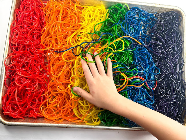 rainbow spaghetti in a baking dish with a child's hand playing.
