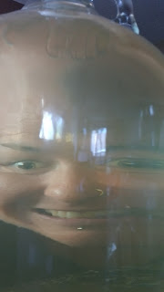 A woman's distorted face as she grins insanely through a gallon jug of homemade wine.