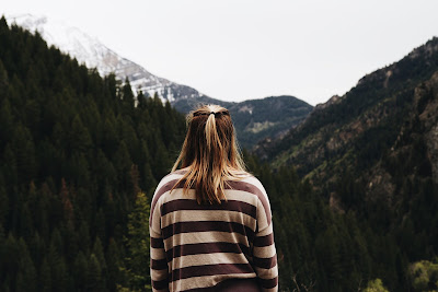 Girl with blonde hair looks at the forest covered mountains