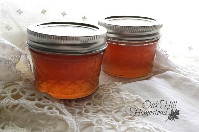 Rose petal jelly in two 4-oz canning jars on a white lace-covered tabletop.