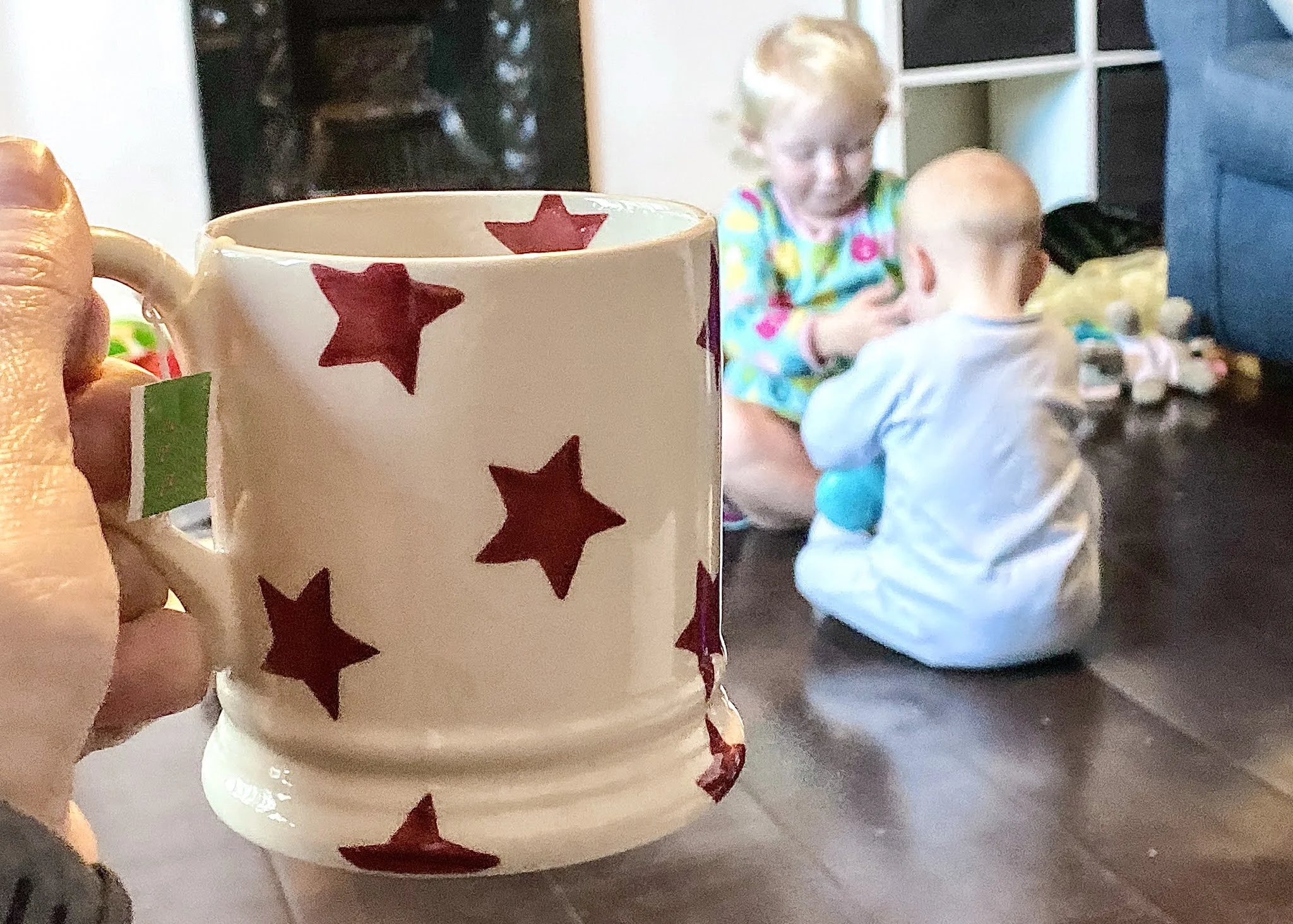 A cup of tea being held with children playing in the background in a low maintenance to clean and tidy house