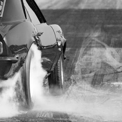 A black Chevrolet Camaro spinning it's rear wheels doing a burnout at the beginning of a drag race.