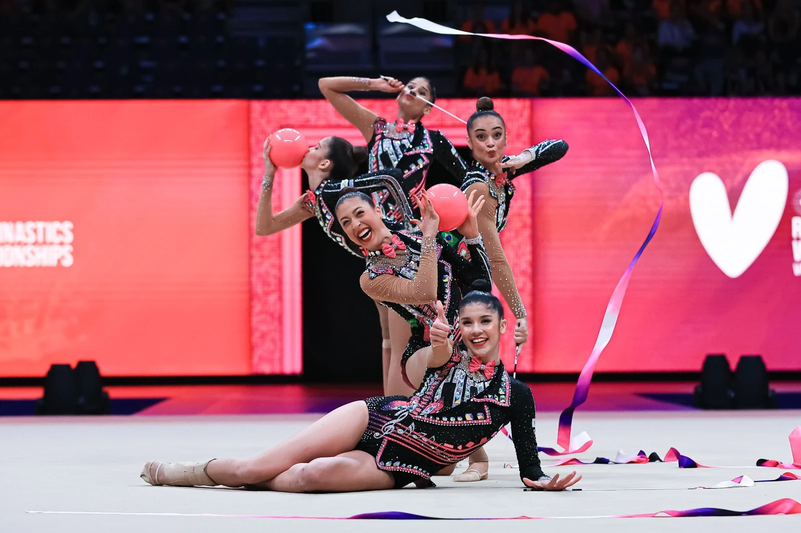 Com collant preto, Duda está deitada na frente das meninas e faz um sinal de positivo no final da coreografia