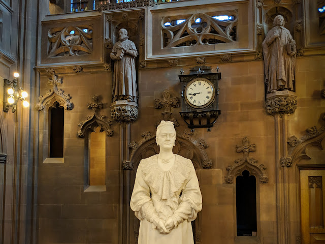 white marble statue in front of gothic interior including clock and two small statues