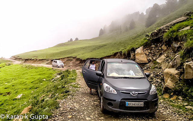 Hello everyone. I may not be good with words but somehow I am going to share about one of the most exciting and memorable trip I had with my family during monsoons of 2012The destination was Prashar lake, situated at a height of 2730 meters above sea level, 49 km north of Mandi, a buzzling town situated in Himachal Pradesh. It’s a place about which very few people know, but once anyone visits Prashar, he longs to come back againFor convenience of visiting tourists, recently HPPWD and HP Forest Department constructed different rest houses. In addition a Trekker’s Lodge was also constructed which is more sophisticated than othersThe bookings can be done from respective offices in MandiAfter making all the necessary arrangements including food etc. , we a group of 15 family members started from Mandi at about 4 pm. It was a risk though in monsoons because almost 25 km of road was a muddy tarmac and had become slippery, thanks to some contractor who didn’t do a good jobAs we came closer to our destination, more the chill in air increased. This was my second visit to Prashar. Earlier I had trekked almost 14 kms to reach there way back in year 2000. The route chosen was via Katindi, Kataula and last thickly populated place en route is Baghi, which is 28 kms from Mandi approximately. Till here the road condition is good. After crossing Baghi you will find lesser number of inhabitants. As you move higher, just 5 km before Prashar you will find one room mud & stone houses, inhabited by shepherds or gaddi’s as they are locally knownWe reached Prashar at 7 pm as last 14 kms of distance had to be covered in fog. The temperature was a whooping 2 degrees celcius in evening. After some tea everyone settled down in quilts and blankets, as that was no doubt the need of hour. With fog and darkness all around there was nothing to be explored nearby, so after a tasteful dinner I sleptI woke at around 6 am in morning. The scenery outside was mesmerizing. It had rained during night. The clouds were making way for mountains to be seen. The cold didn’t stop me from getting my camera and go for a short exploration spree around. The surroundings were full of many types of flowers. The area had various types of flora.At around 8 am it started raining again, and that is when I noticed one of our cars had a flat tyre. It was replaced then and there as chances of heavy rainfall were expected in later part of the day. At such places there are no workshops etc. so one has to come well prepared beforehandOnce all were ready luckily it stopped raining. We all started for the famous Prashar Rishi Temple and Lake. It’s a 15 minute walk from the rest house when you reach and gaze down to see a lake having crystal clear water and a temple premises consisting of three pagoda architecture buildingsThe myth about Prashar Lake is that it was formed after Saint Rishi performed meditation hereThe depth of the lake is still uncertain. Rumors are that the main temple is beneath the lake.  It is also said that there is a big treasure beneath the lake, but no one dares to go and find out. Once some foreign national took a dip in lake to reach the depth.  It is said that once he returned he lost his visionBeing a Sunday the secluded place was abuzz with activity with many tourists thronging to seek blessing and enjoy their SundayOne can make out that how much worshipped diety is Prashar Rishi as large number of followers were seen seeking blessingsThere are two shops which serve delicious rajmah-rice and tea in vicinity of lakeAs the day was foggy, the beauty of Lake was at its bestOne must surely visit the place.