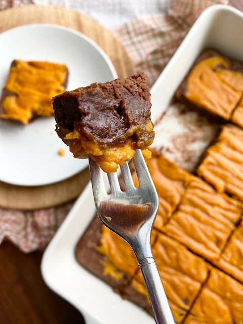 A bite of a pumpkin brownie on a fork with a tray of brownies in the background.