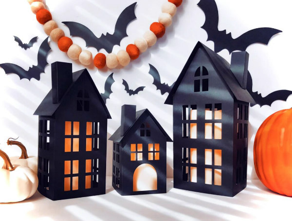 three black houses displayed with bats, white and orange pumpkins, and felt ball garland