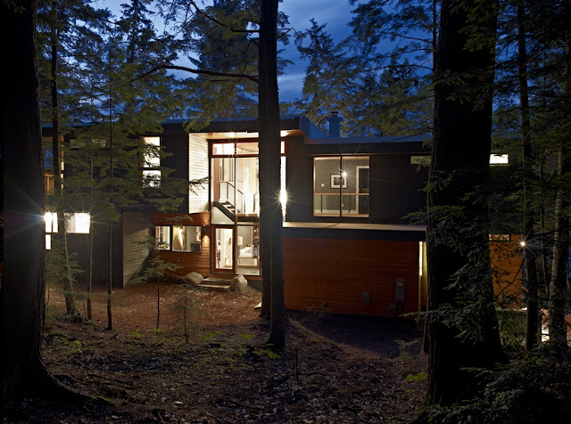 Photo of the forest house with lights turned on as seen from the forest