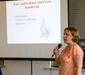 Foto van een presentatie over inclusief MVO en werk, waar Bianca met een microfoon in de hand sta en een Power Point op de achtergrond. 