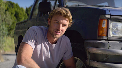 Adam Demos crouches down next to his truck to assess the damage in a still for Netflix's original film Falling Inn Love (2019)