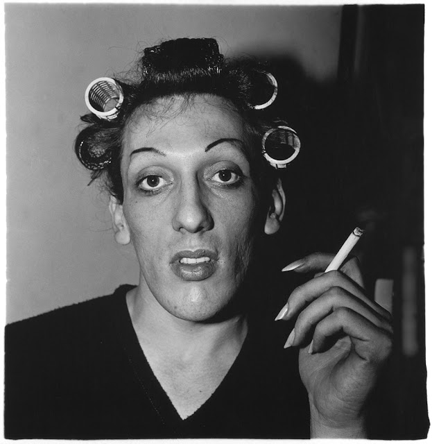 Foto em preto e branco, retratando um homem, com rolos no cabelo,  segurando um cigarro na mão olhando para a frente