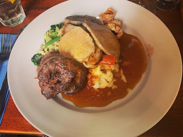 Roast dinner of pork, yorkshire pudding, and vegetables, covered in gravy