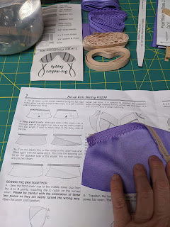 Hand holding piece of bra in progress next to pattern instructions