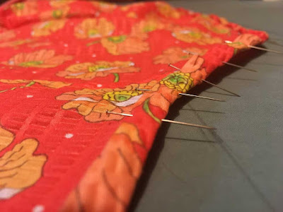 A close-up of a neatly pinned bound edge in bright coral fabric with an orange poppy flower print.
