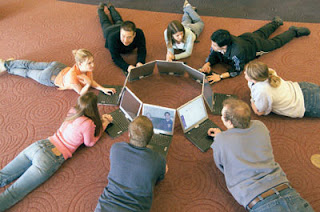 Children sitting in a circle on the floor using computers.