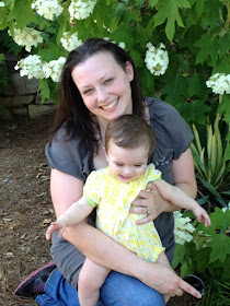 Mom and baby sharing a happy moment next to a flowering bush.