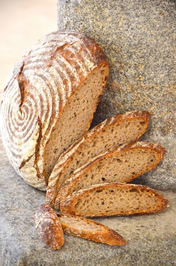 Ein Laib Brot steht angelehnt an eine Steinsäule. Einige Scheiben sind bereits abgeschnitten und liegen fächerförmig davor.